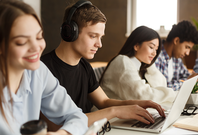 Two young men and two young women studying. One young man is typing on this computer.
