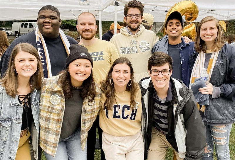 A group of young male and women standing together while smiling to the camera.