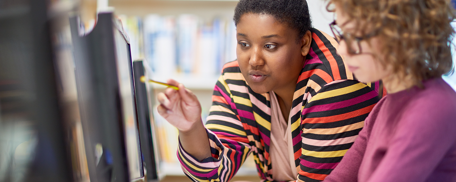 A Black woman and a white one look at a computer screen.